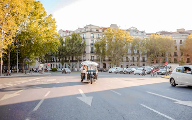 Electric tuk-tuk driving through a tree-lined street in Madrid.