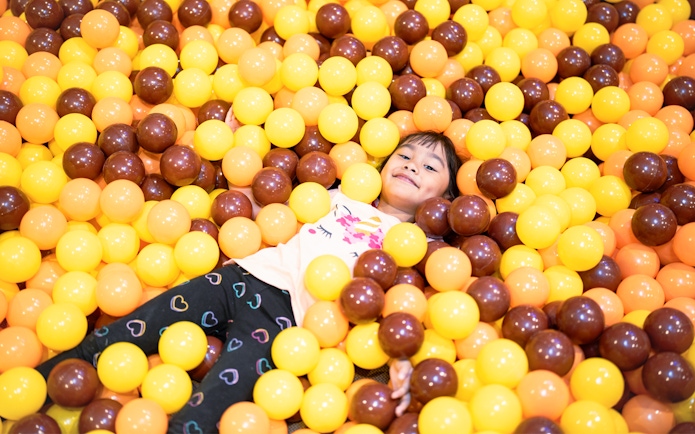 Child playing in a ball pit filled with yellow and brown balls.
