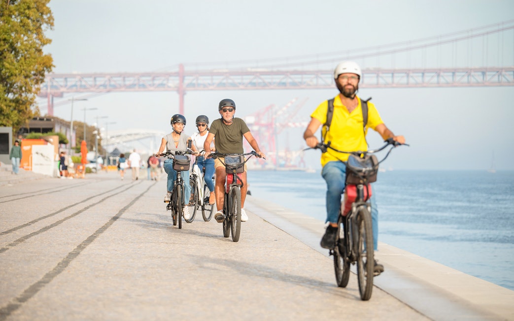 Cyclists ride along the waterfront under Lisbon's 25th of April Bridge.