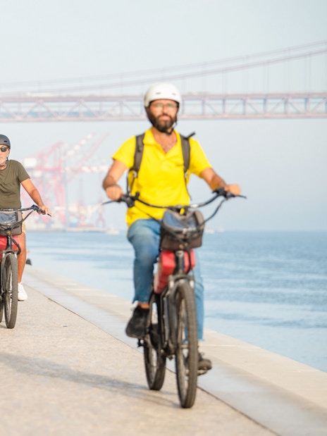 Cyclists ride along the waterfront under Lisbon's 25th of April Bridge.