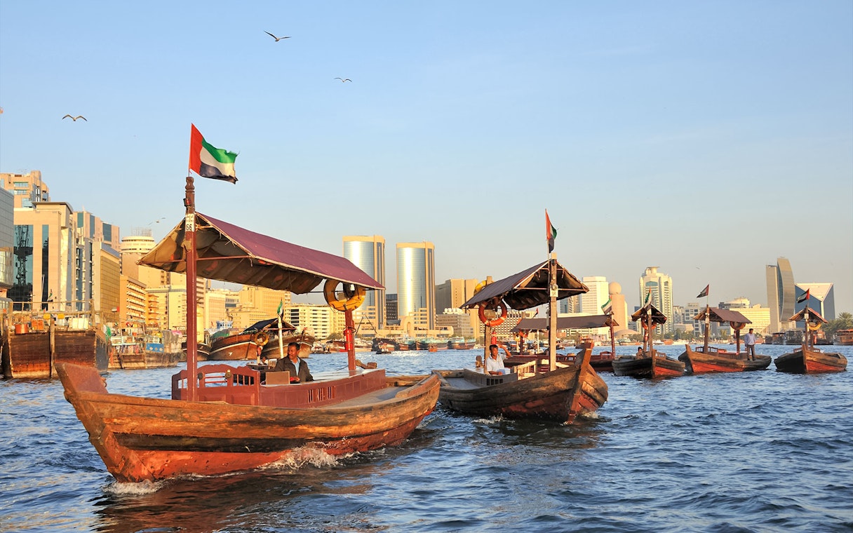 Traditional wooden boats on Dubai Creek with city skyline in the background.