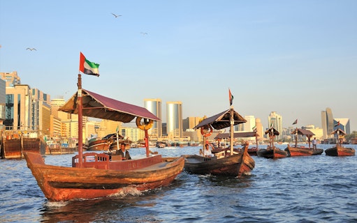 Traditional wooden boats on Dubai Creek with city skyline in the background.