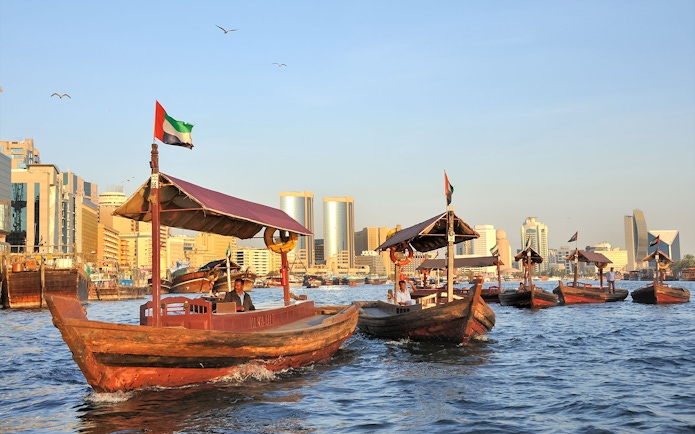 Traditional wooden boats on Dubai Creek with city skyline in the background.