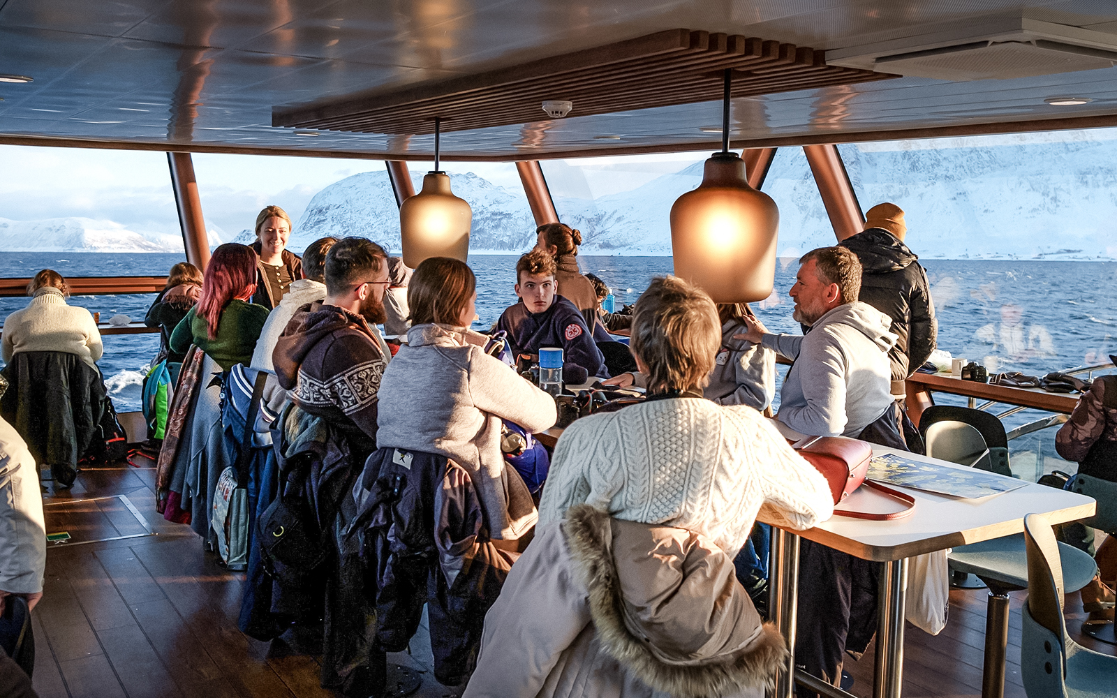 Tourists enjoying a scenic Arctic fjord cruise from Tromso with snowy mountains in the background.