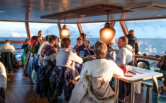 Tourists enjoying a scenic Arctic fjord cruise from Tromso with snowy mountains in the background.