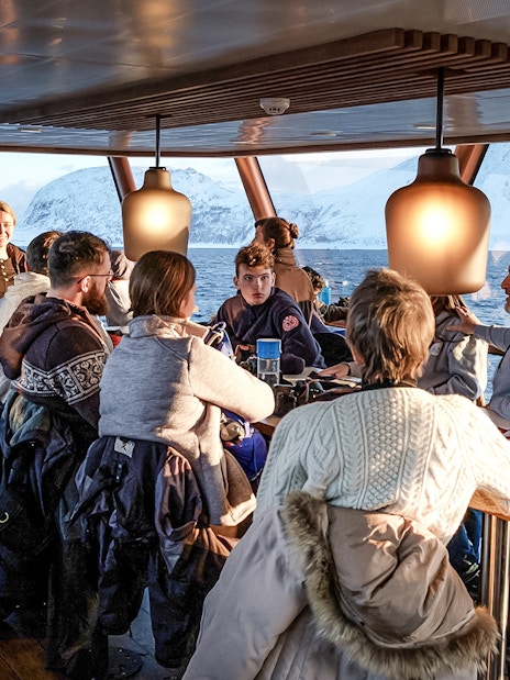 Tourists enjoying a scenic Arctic fjord cruise from Tromso with snowy mountains in the background.