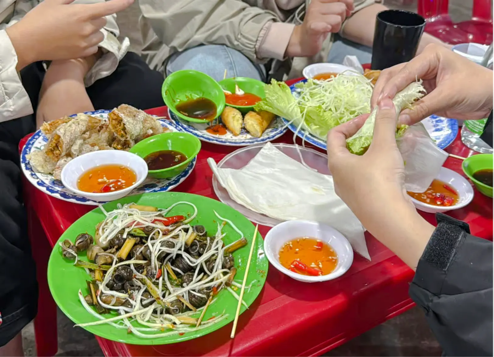 Hands preparing Vietnamese spring rolls with fresh vegetables and dipping sauces in Da Nang.