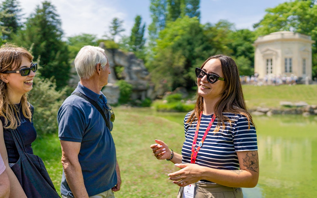 Tour guide explaining Petit Trianon to tourists in Versailles garden.