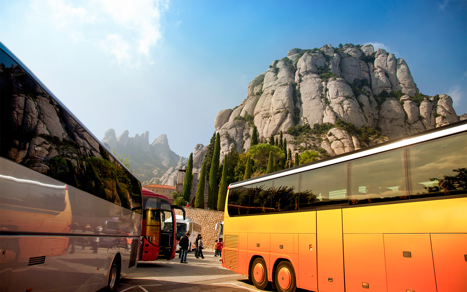 Tour bus parked at Montserrat, Spain, with scenic mountain backdrop.