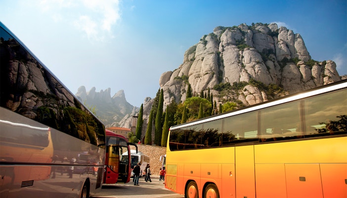 Tour bus parked at Montserrat, Spain, with scenic mountain backdrop.