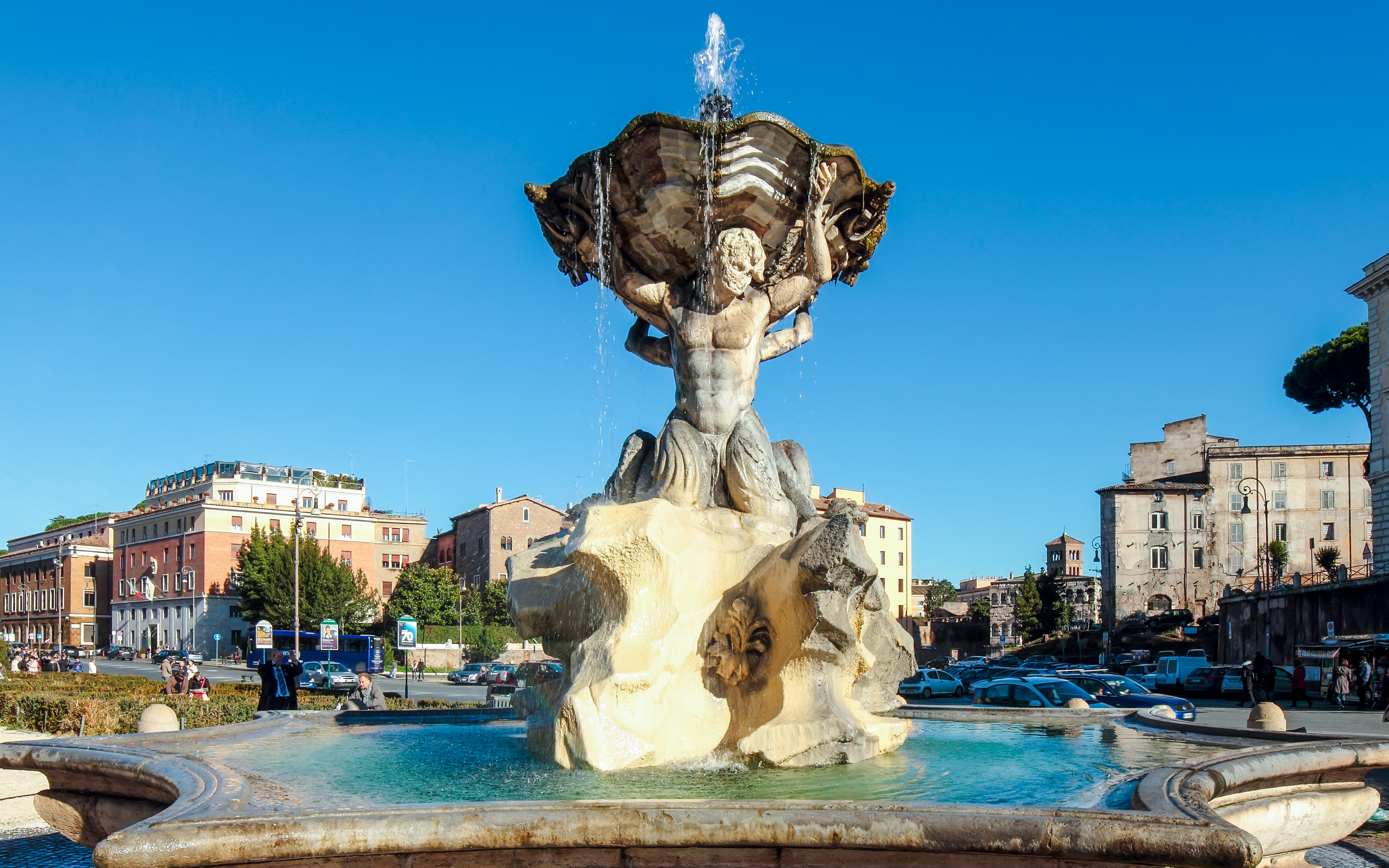 Fountain of the Tritons in Rome with surrounding buildings and clear sky.