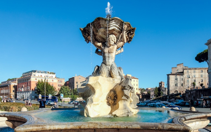 Fountain of the Tritons in Rome with surrounding buildings and clear sky.