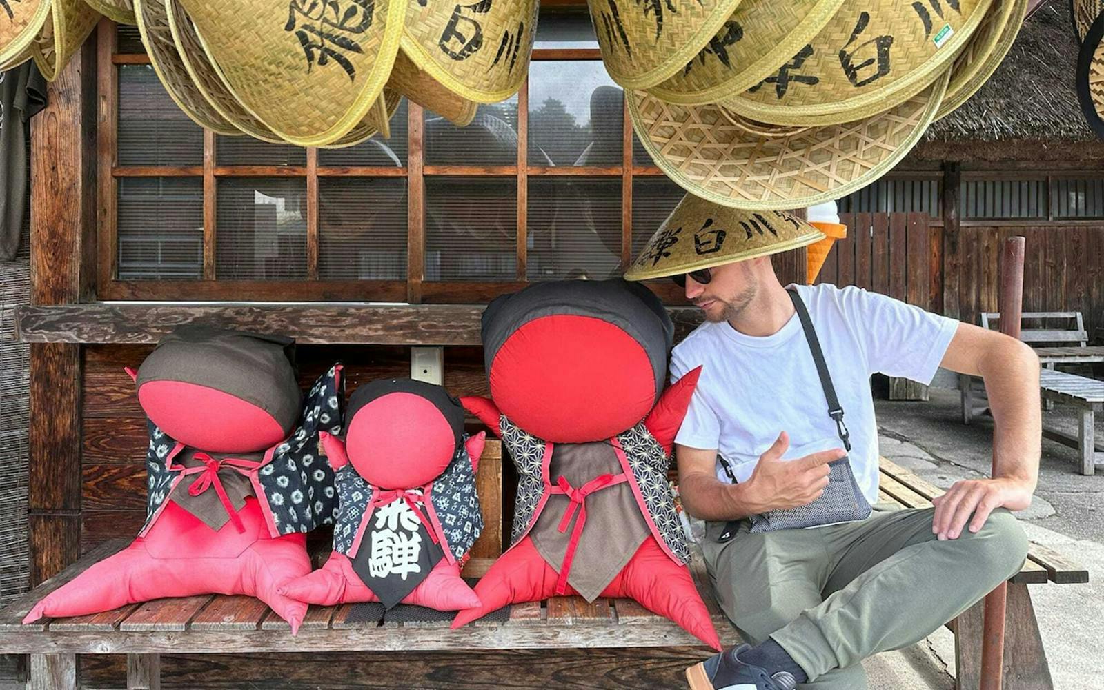 Man sitting with traditional Japanese dolls and straw hats in Shirakawa-go.