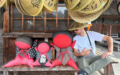 Man sitting with traditional Japanese dolls and straw hats in Shirakawa-go.
