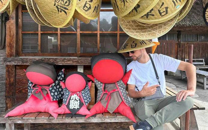 Man sitting with traditional Japanese dolls and straw hats in Shirakawa-go.