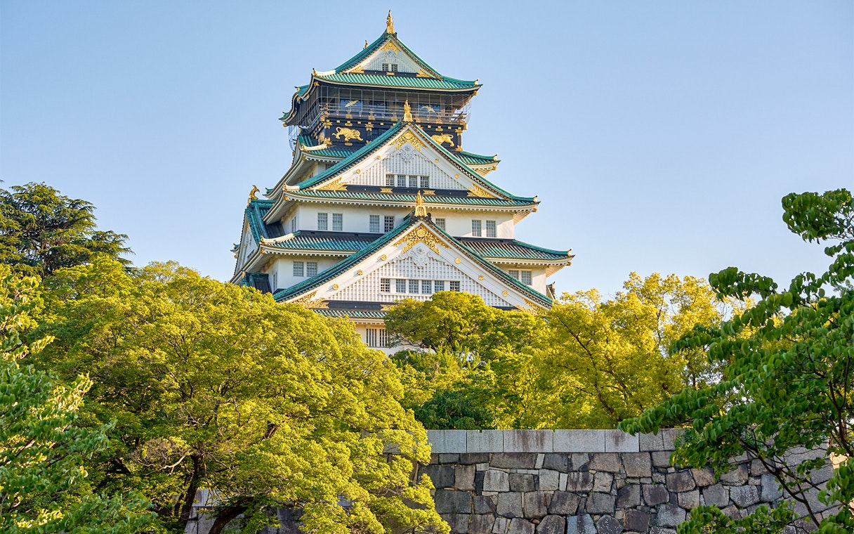 Osaka Castle exterior with lush green trees and blue sky.