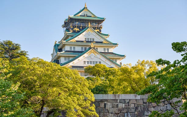Osaka Castle exterior with lush green trees and blue sky.