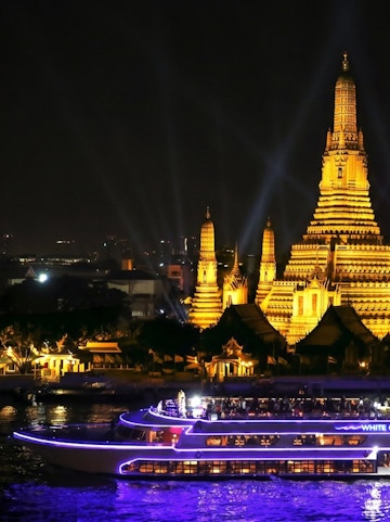 Cruise boat on Chao Phraya River with Wat Arun temple illuminated at night, Bangkok.