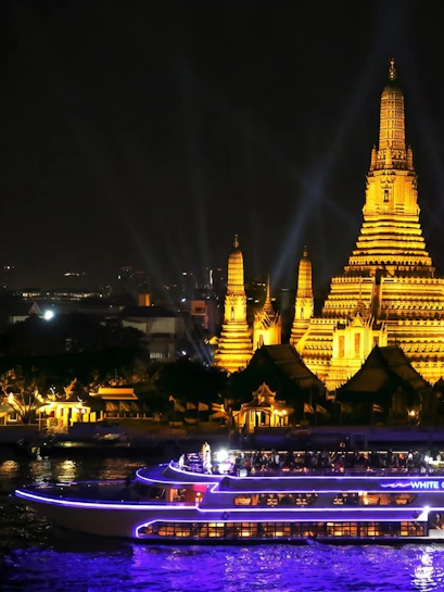 Cruise boat on Chao Phraya River with Wat Arun temple illuminated at night, Bangkok.