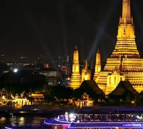 Cruise boat on Chao Phraya River with Wat Arun temple illuminated at night, Bangkok.