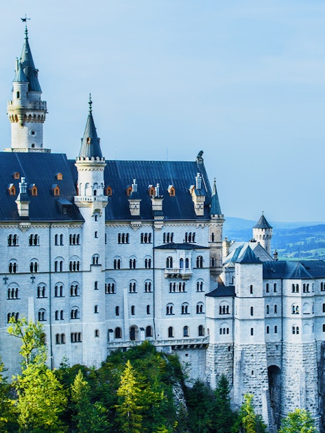 Neuschwanstein Castle in Bavaria, Germany, surrounded by lush greenery and distant hills.