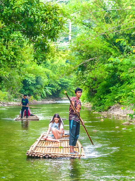 Bamboo rafting on a lush green river surrounded by dense foliage.