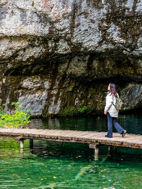Female walking on wooden deck over turquoise water at Plitvice Lakes, Croatia.