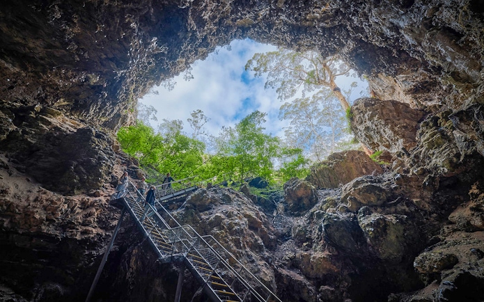 Stairs leading up from Lake Cave sinkhole entrance, Margaret River, with trees and sky above.
