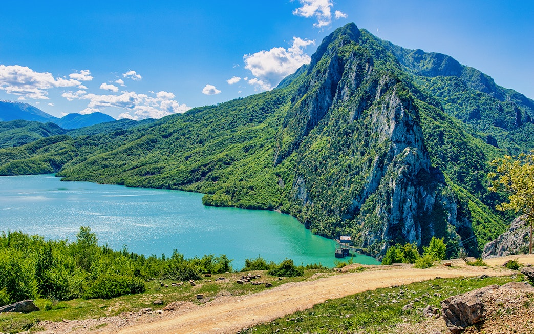 Bovilla Lake with surrounding green mountains and clear blue sky.