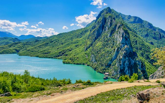 Bovilla Lake with surrounding green mountains and clear blue sky.
