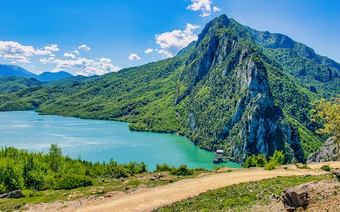 Bovilla Lake with surrounding green mountains and clear blue sky.