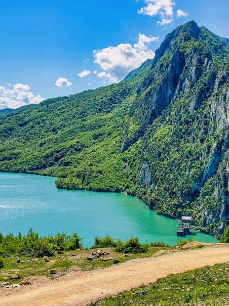 Bovilla Lake with surrounding green mountains and clear blue sky.