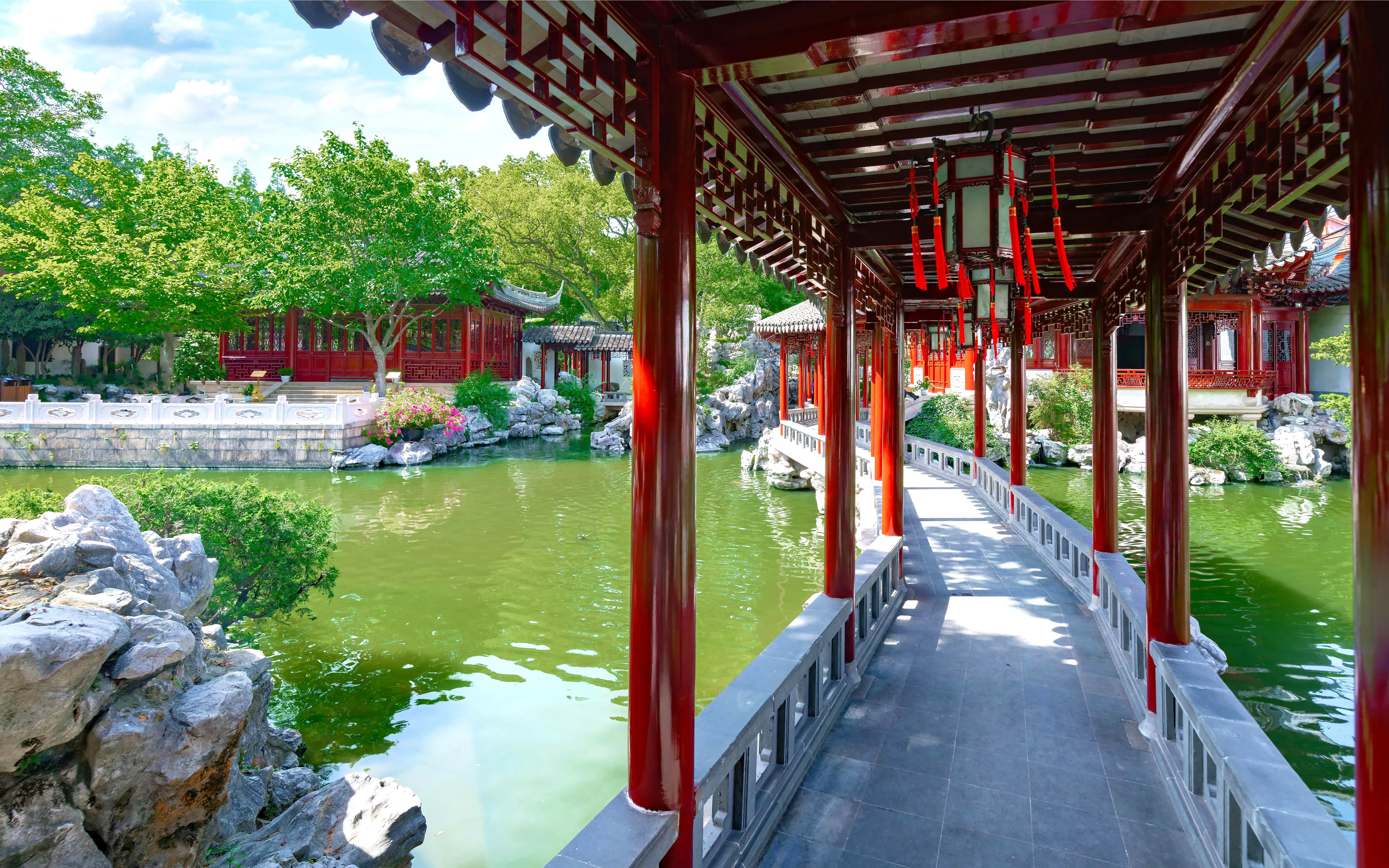 Covered walkway over pond in Yu Garden, Shanghai, China, with traditional architecture and lush greenery.