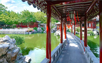 Covered walkway over pond in Yu Garden, Shanghai, China, with traditional architecture and lush greenery.