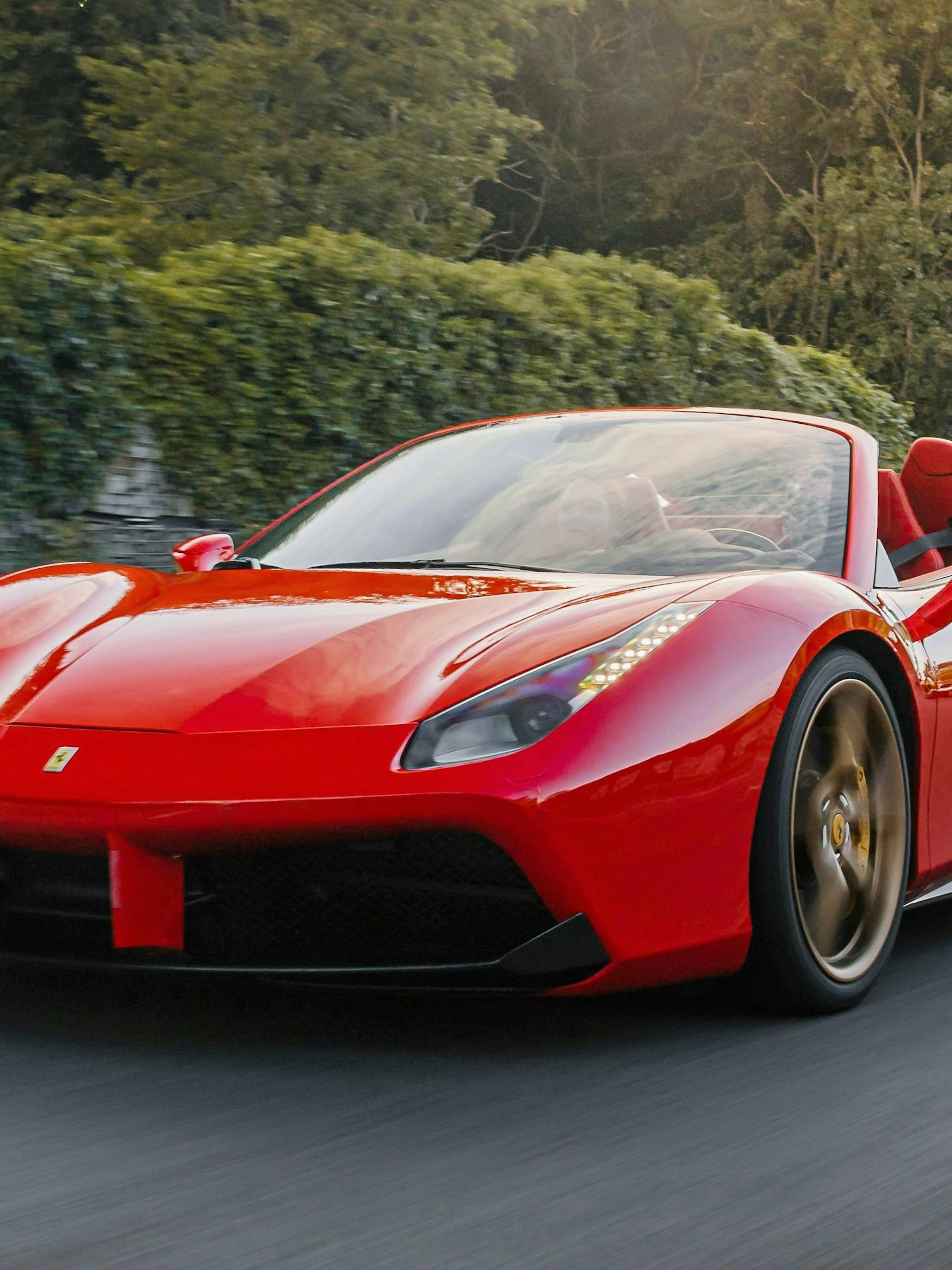 Red Ferrari driving on a scenic road with lush greenery in the background.