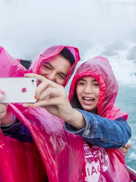 People in pink ponchos taking a selfie on a boat near Niagara Falls.