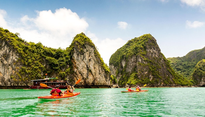 Kayakers paddling in Halong Bay with limestone cliffs in the background.