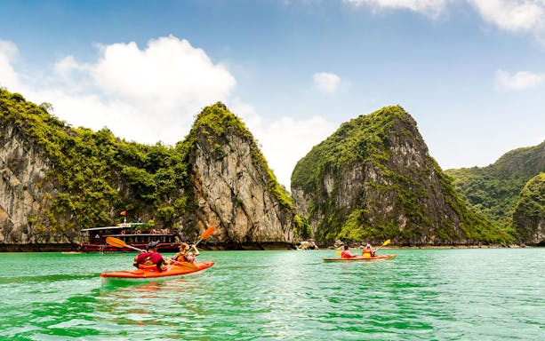 Kayakers paddling in Halong Bay with limestone cliffs in the background.