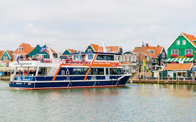 Tourists on a Marken Express boat cruise past colorful Dutch houses in Volendam.