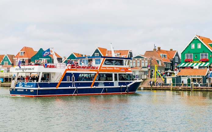 Tourists on a Marken Express boat cruise past colorful Dutch houses in Volendam.