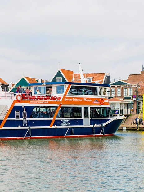 Tourists on a Marken Express boat cruise past colorful Dutch houses in Volendam.