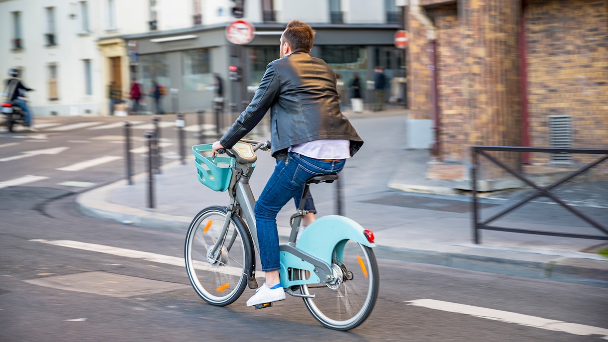 Man cycling on a rented Vélib' bike in Paris near public transport station.