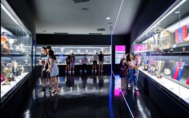 Visitors viewing FC Barcelona trophies in a museum exhibit.