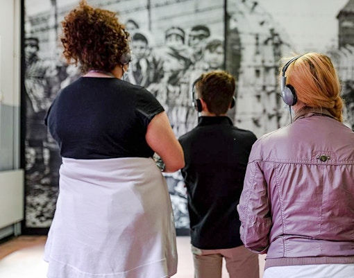 Visitors with headphones viewing Auschwitz Birkenau Memorial Museum exhibit.