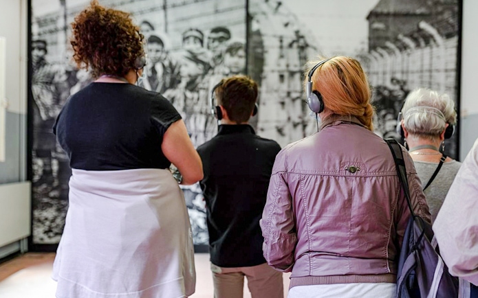 Visitors with headphones viewing Auschwitz Birkenau Memorial Museum exhibit.