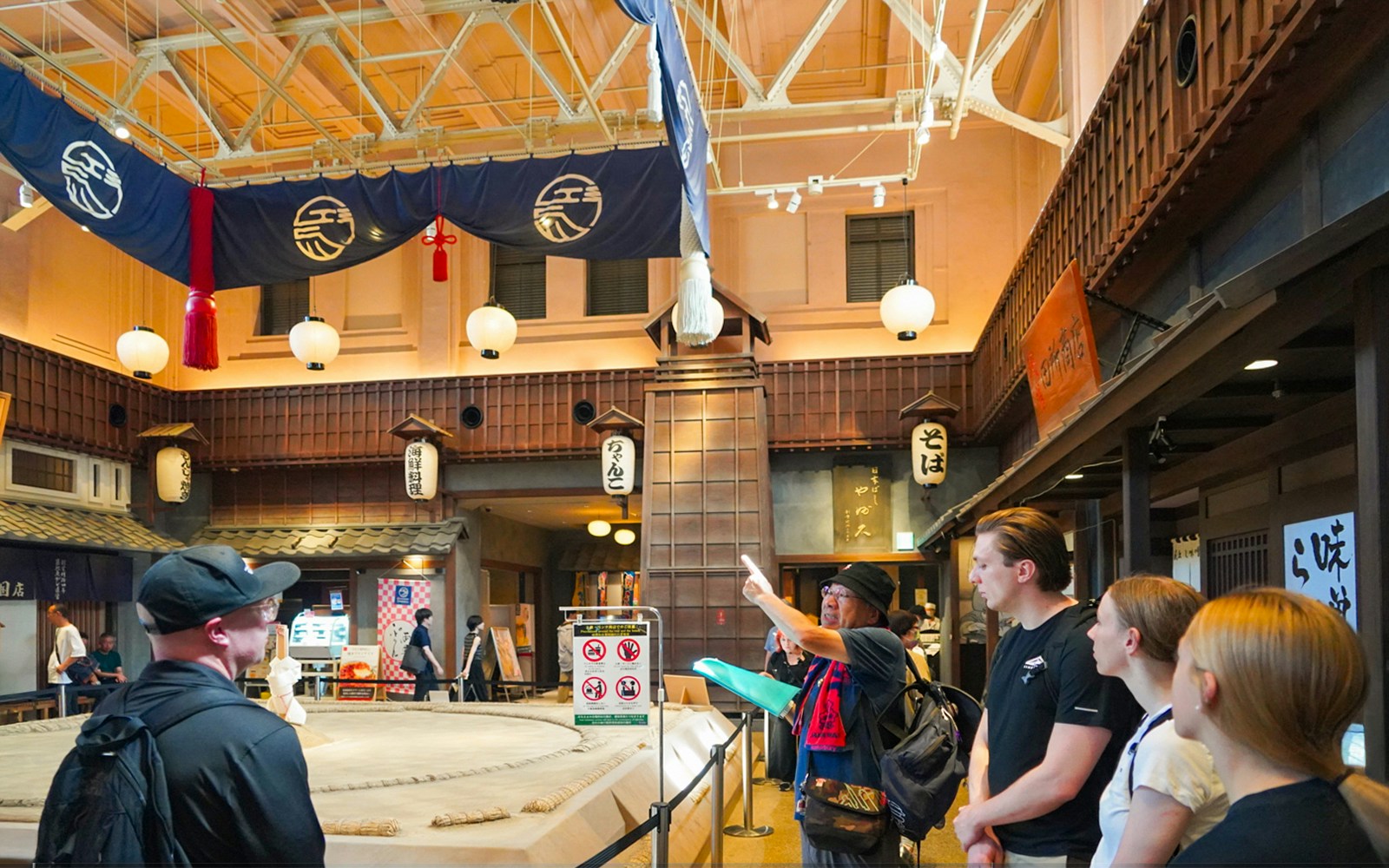 Visitors observing a sumo wrestling ring in Ryogoku, Tokyo, with traditional decor.