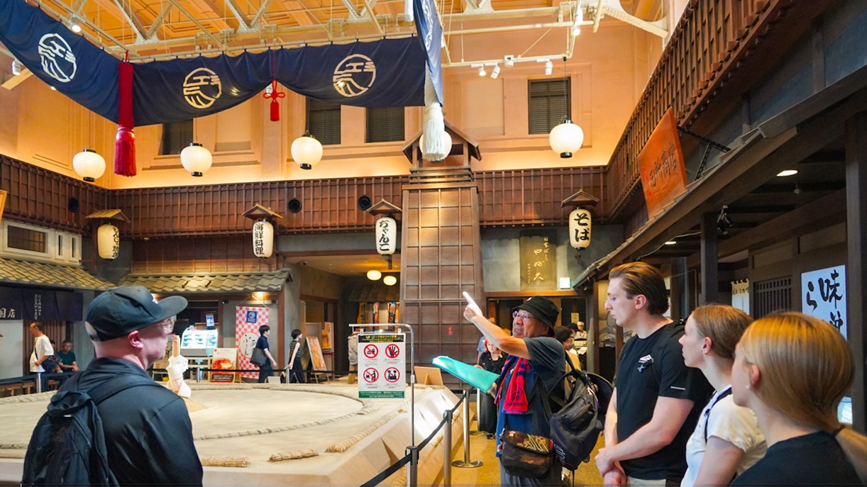 Visitors observing a sumo wrestling ring in Ryogoku, Tokyo, with traditional decor.