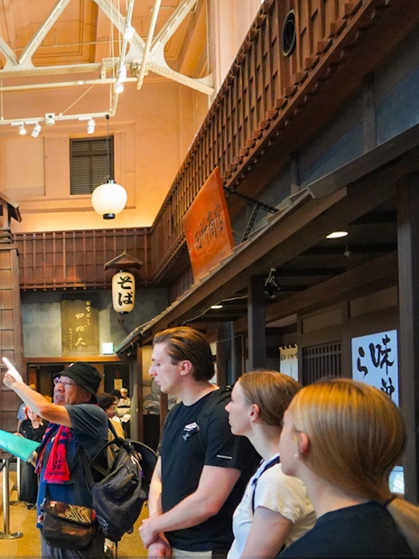 Visitors observing a sumo wrestling ring in Ryogoku, Tokyo, with traditional decor.