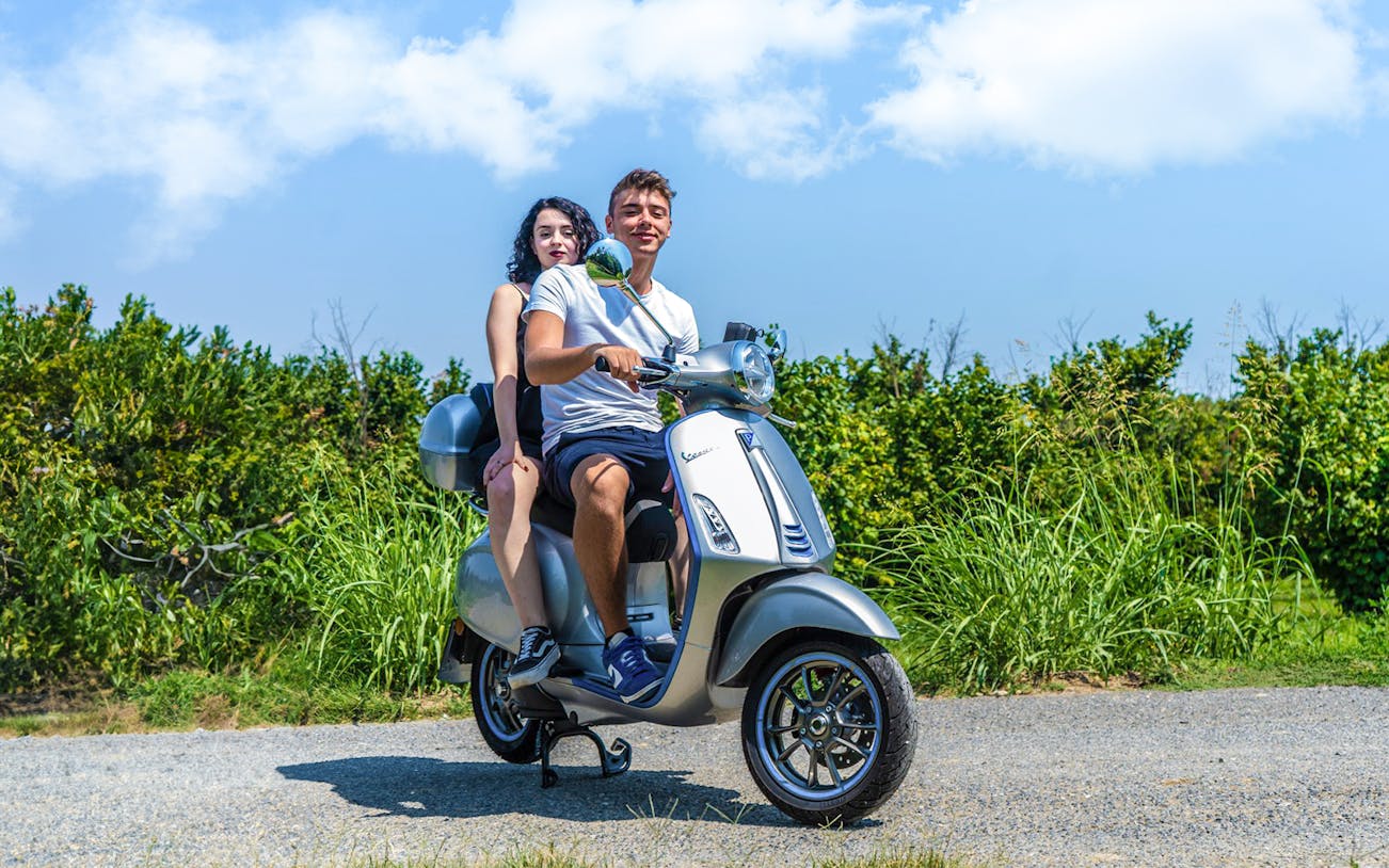 Couple riding a Vespa on a scenic road in Langhe, Italy.