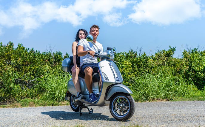 Couple riding a Vespa on a scenic road in Langhe, Italy.